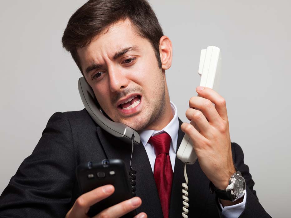 Stressed businessman talking on many phones at once.